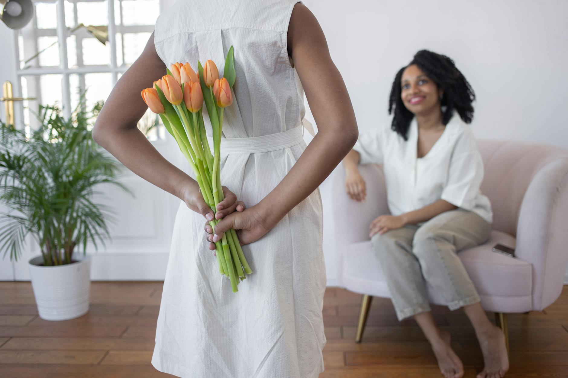A child surprises their mother with tulips indoors, depicting warmth and love.