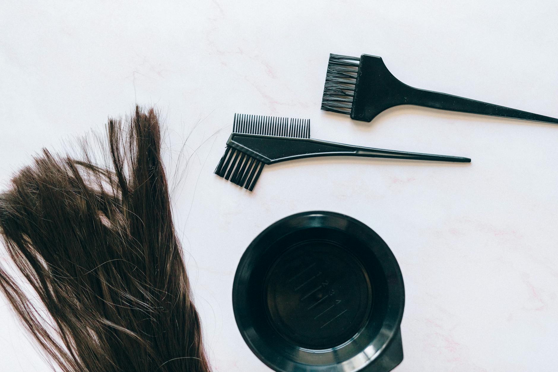 Top view of hair coloring tools and hair strands on a white background.