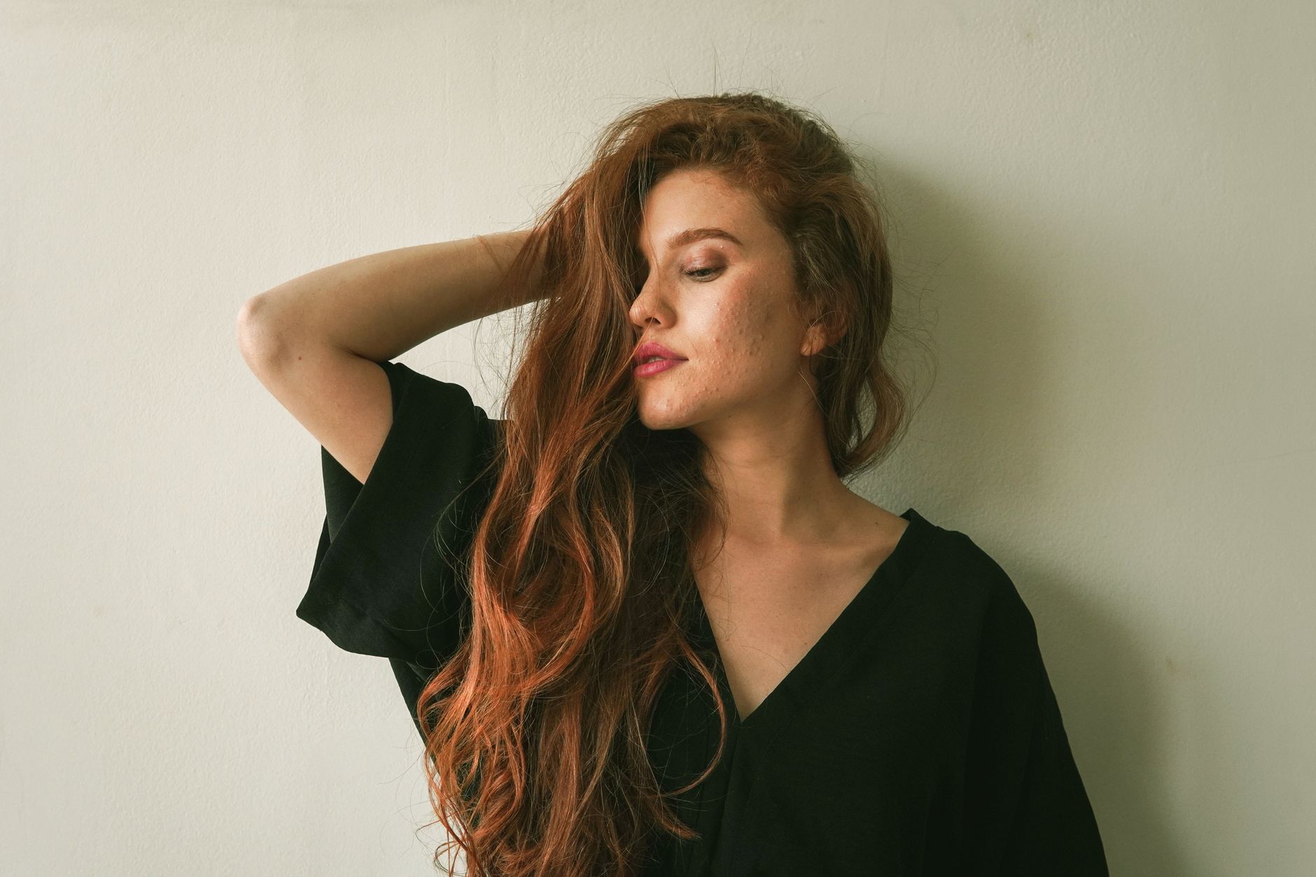 A serene portrait of a woman with long red hair posing gracefully against a plain background.